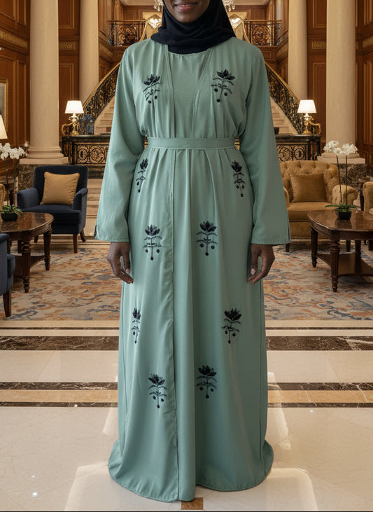 Person wearing a long green dress with floral embroidery against a plain background