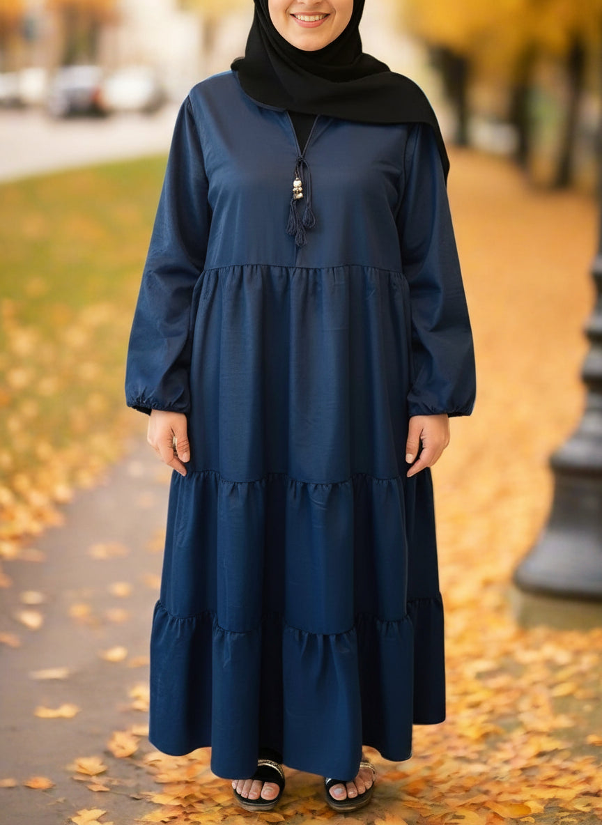 Woman wearing a blue dress with a hijab standing on a leaf-covered path.